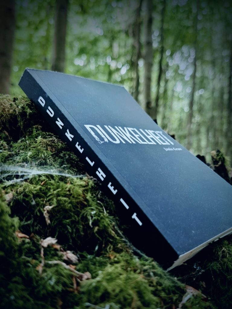 Produktfoto Dunkelheit Ein Buch liegt in einem Erdloch und ist an einigen Stellen von Erde verdeckt.